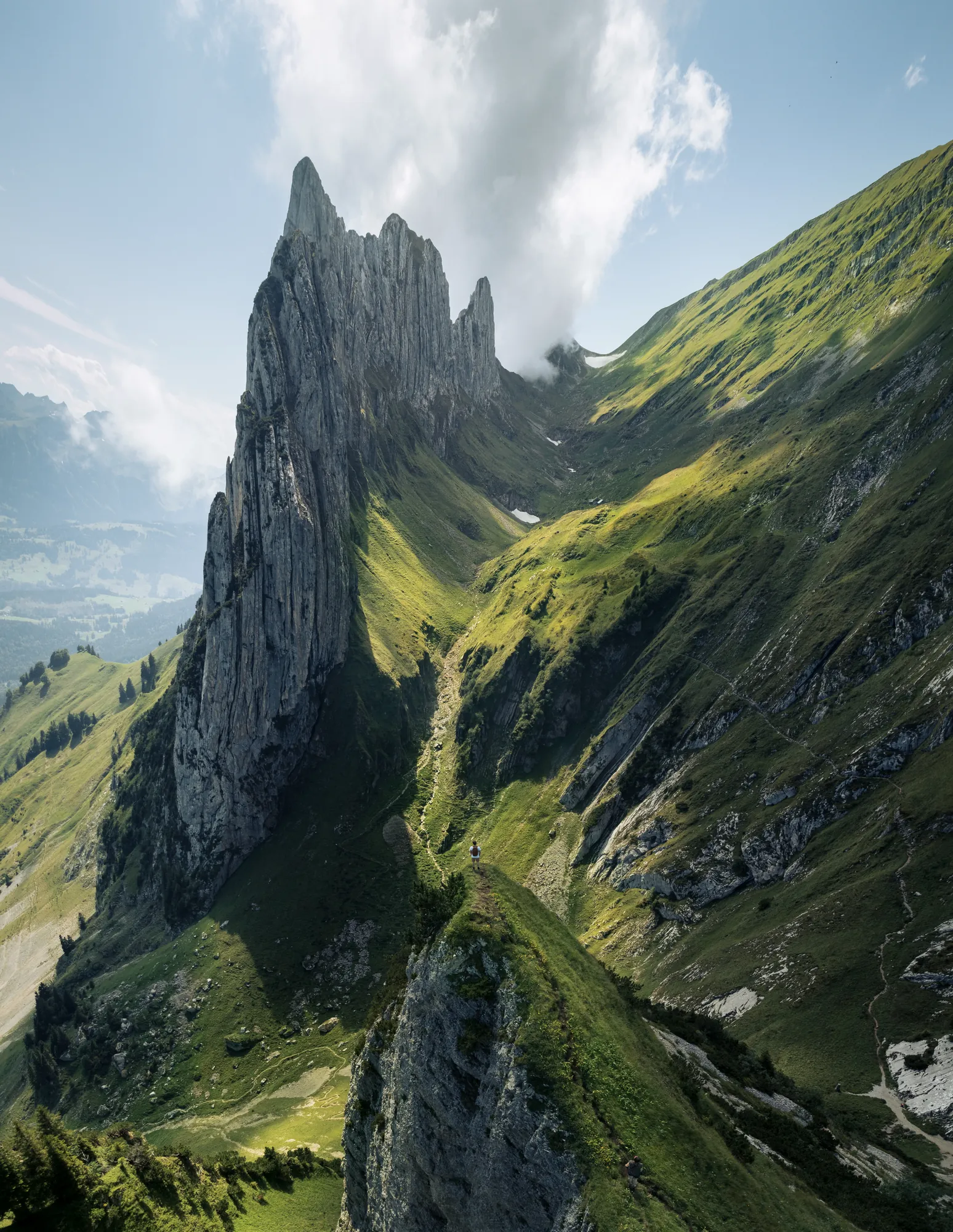 Aerial view of a jagged mountain ridge with steep green slopes and a lone hiker on the path below