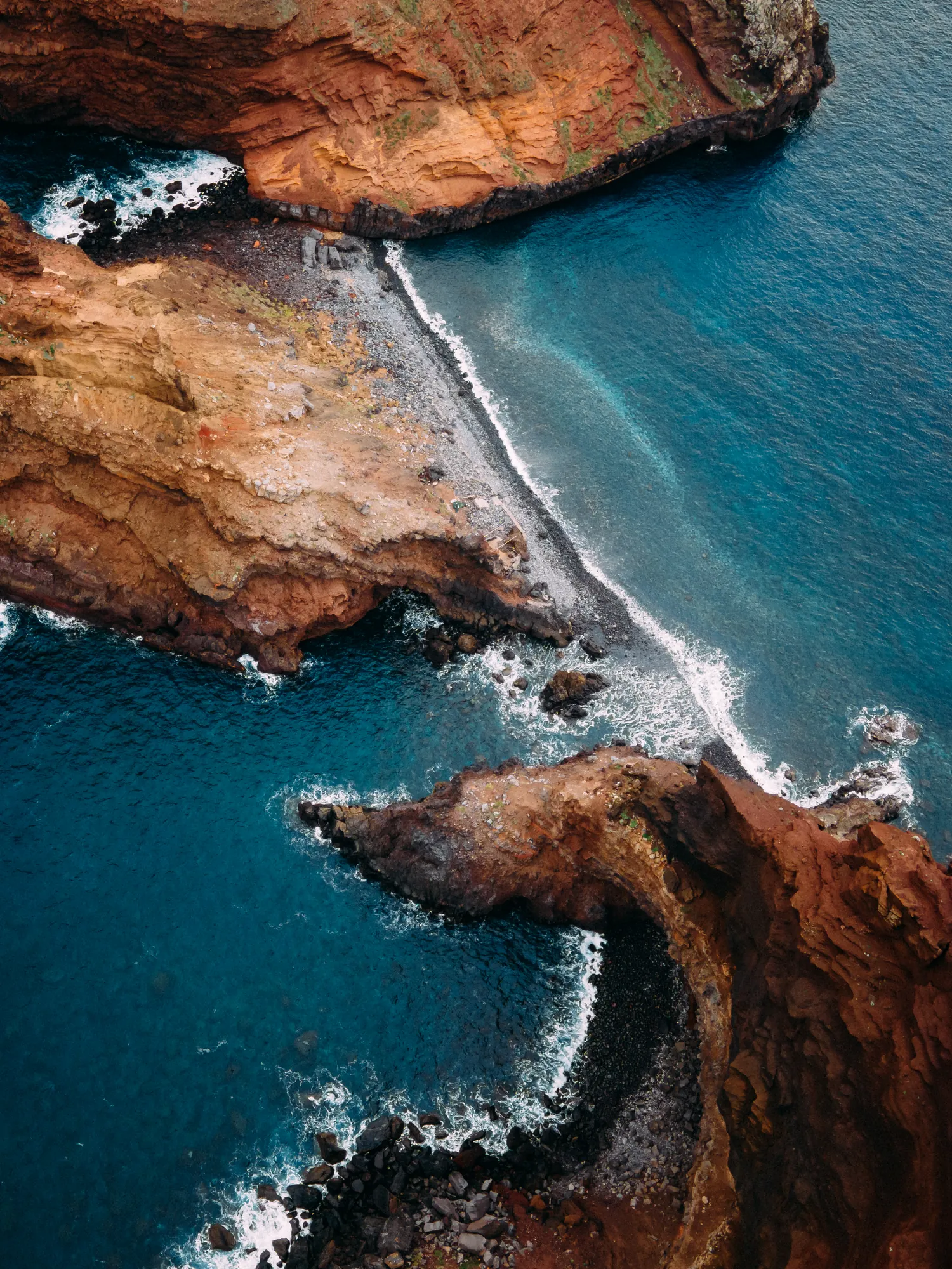Aerial view of red volcanic cliffs meeting deep turquoise water