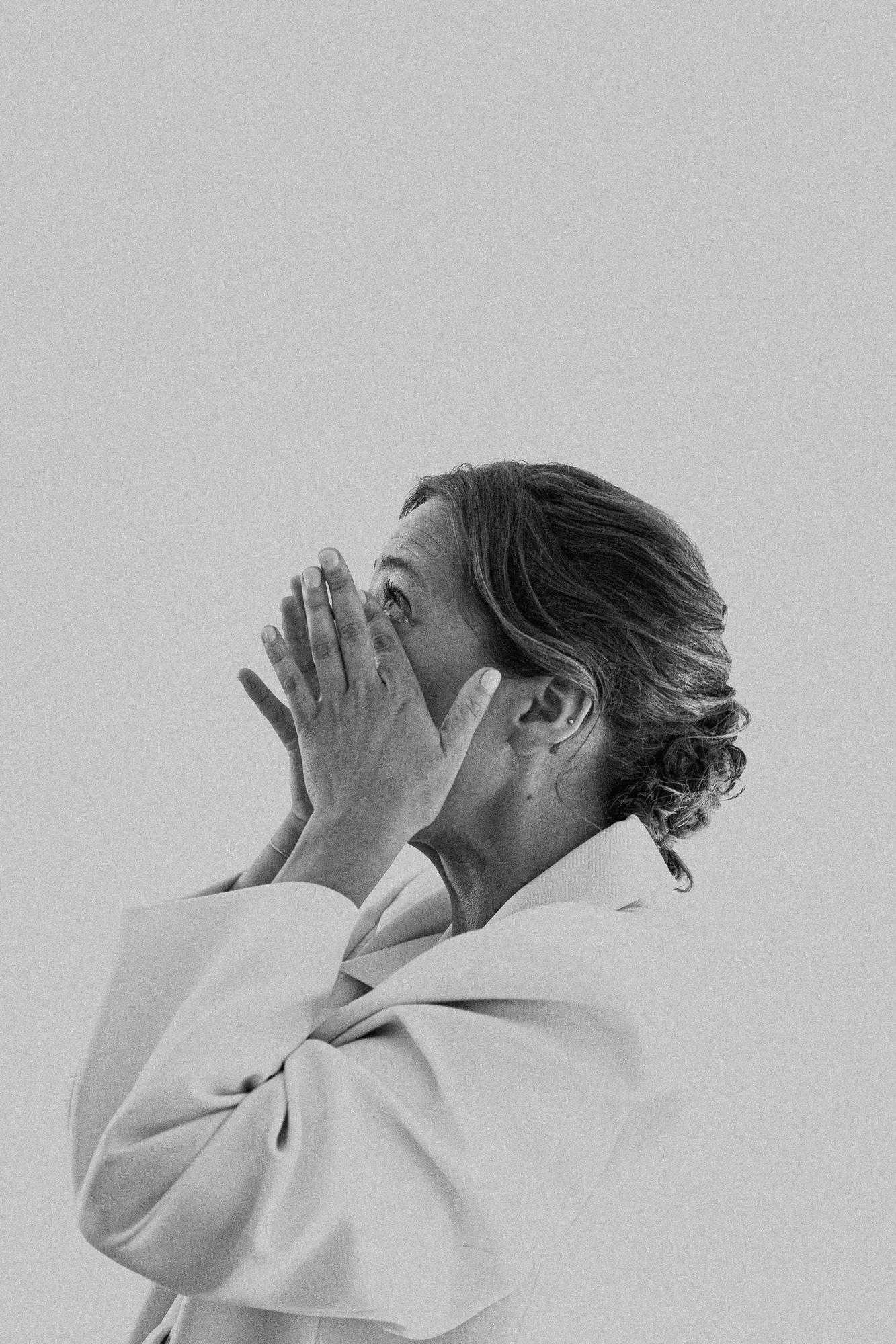 Black and white portrait of a person in a white blazer with hands pressed together at their face
