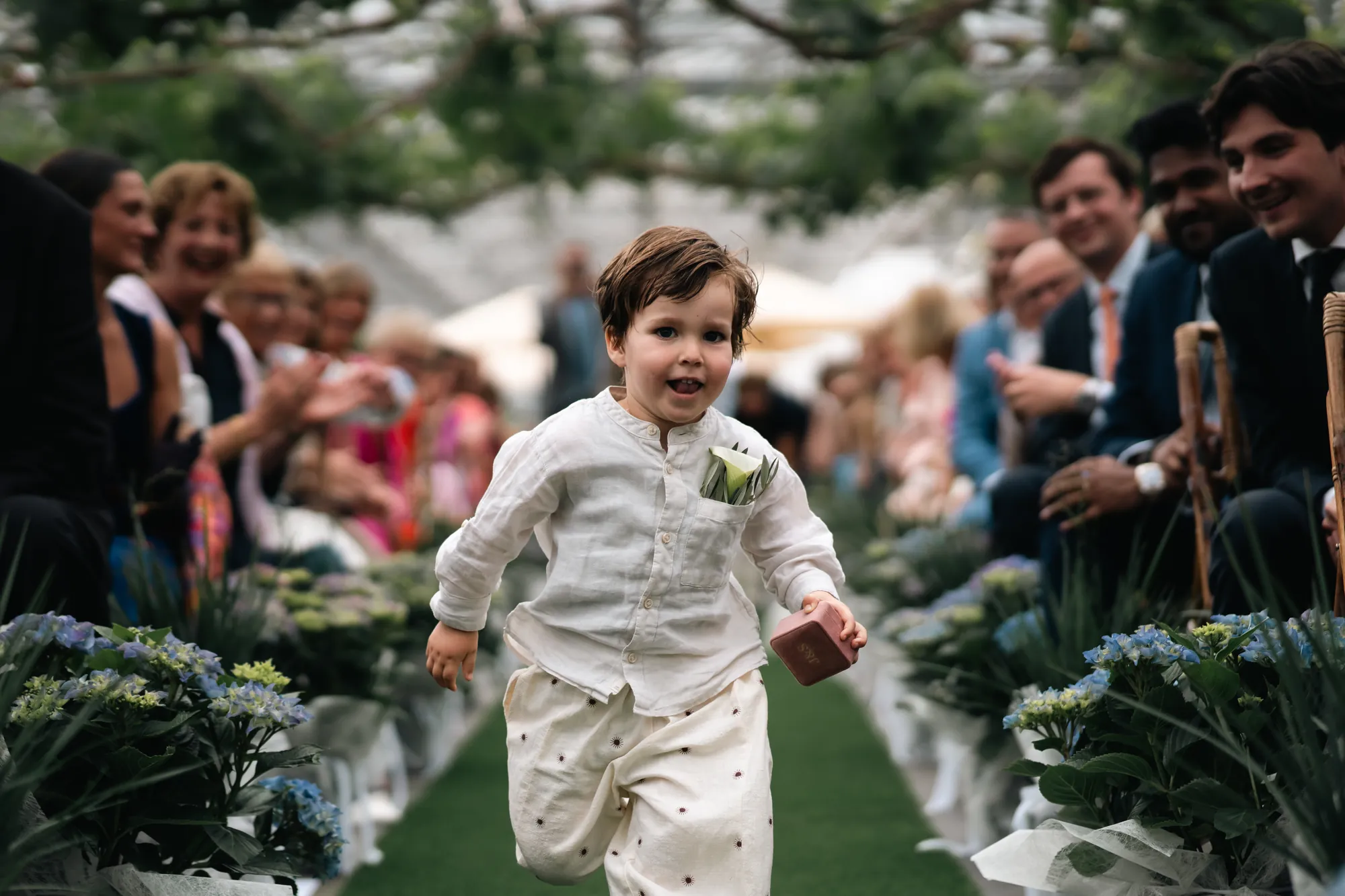 Young child in a white outfit running joyfully down a flower-lined wedding aisle