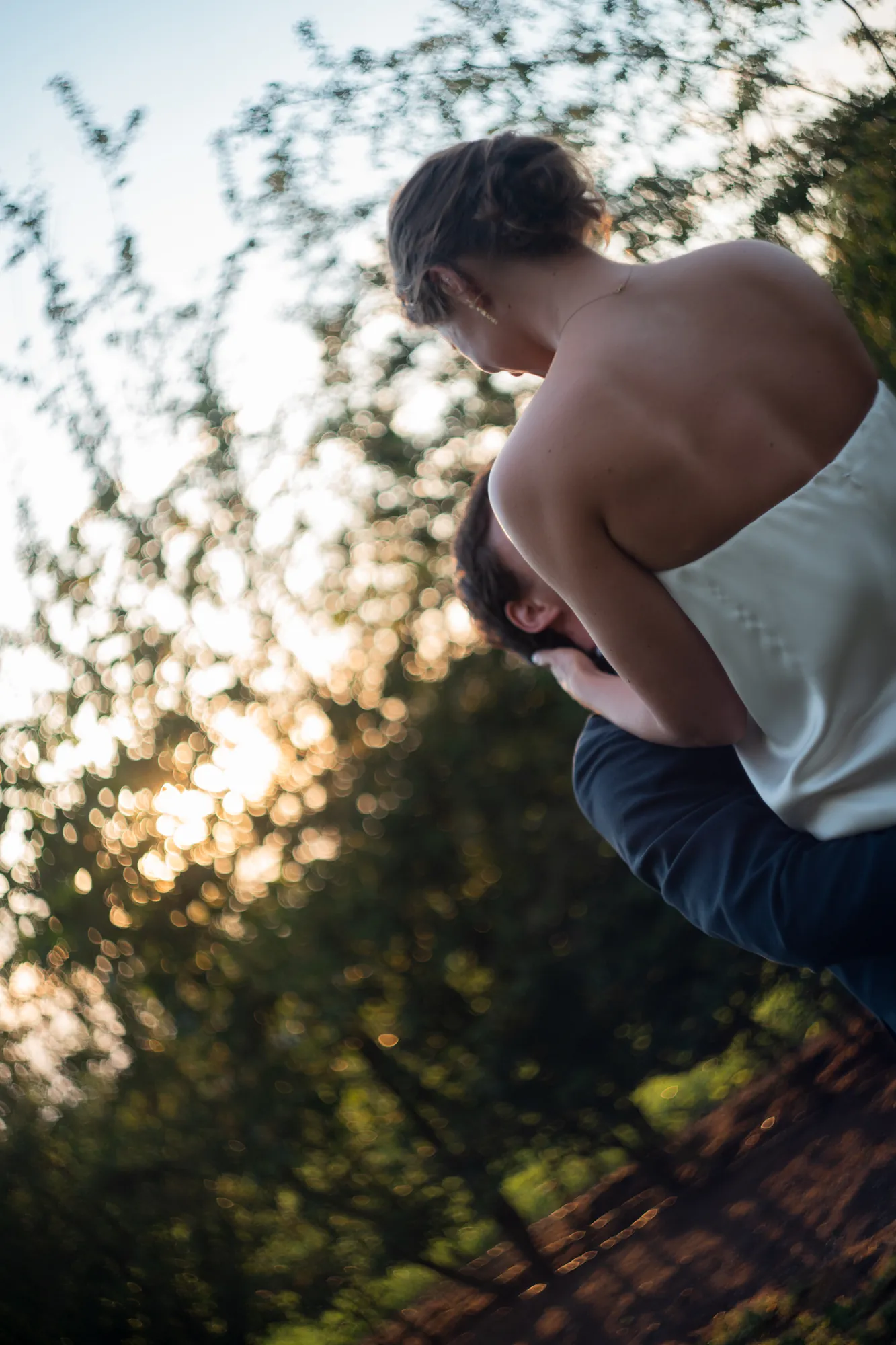 Couple embracing outdoors in soft golden hour backlight, shot from behind
