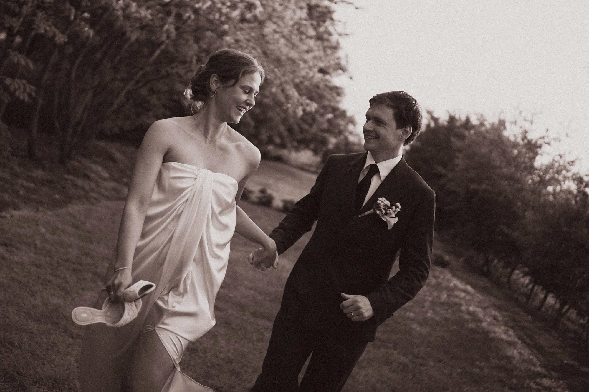 Black and white photo of a bride and groom laughing as they walk hand in hand outdoors
