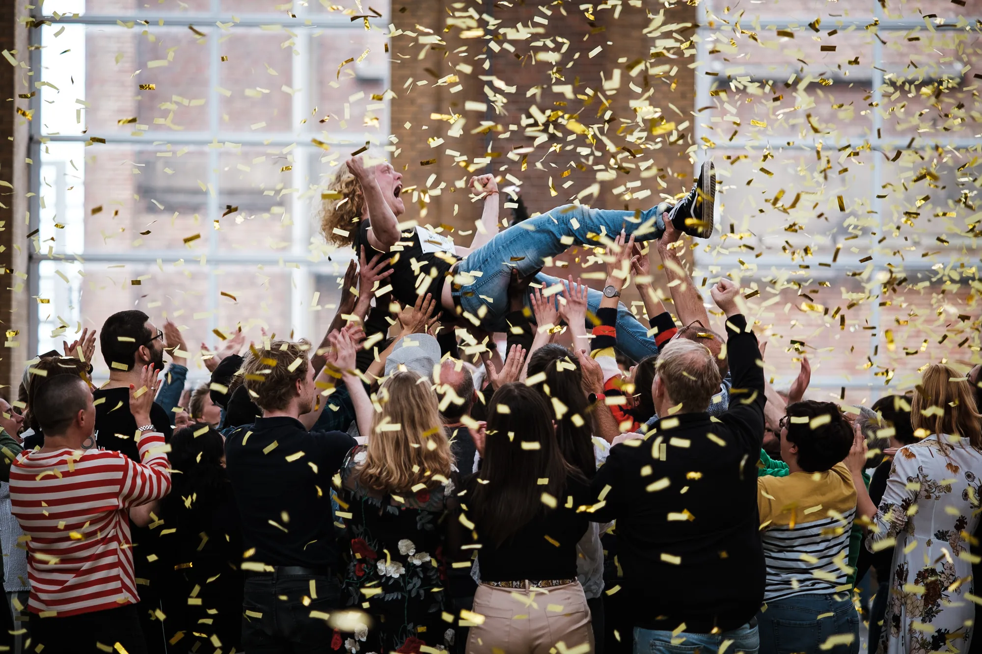 Person crowd surfing above a cheering crowd with golden confetti raining down