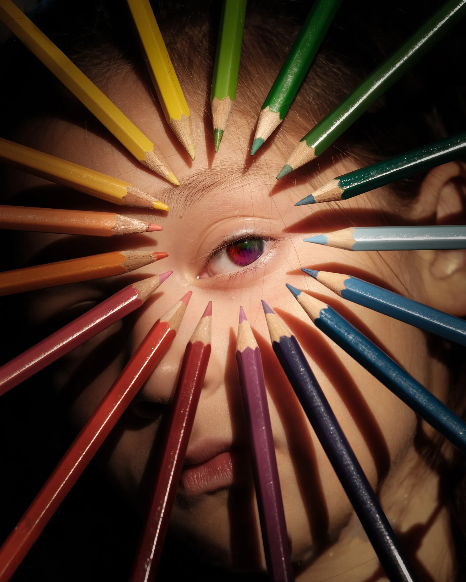 Creative portrait of a woman with colorful pencils radiating outward around her eye