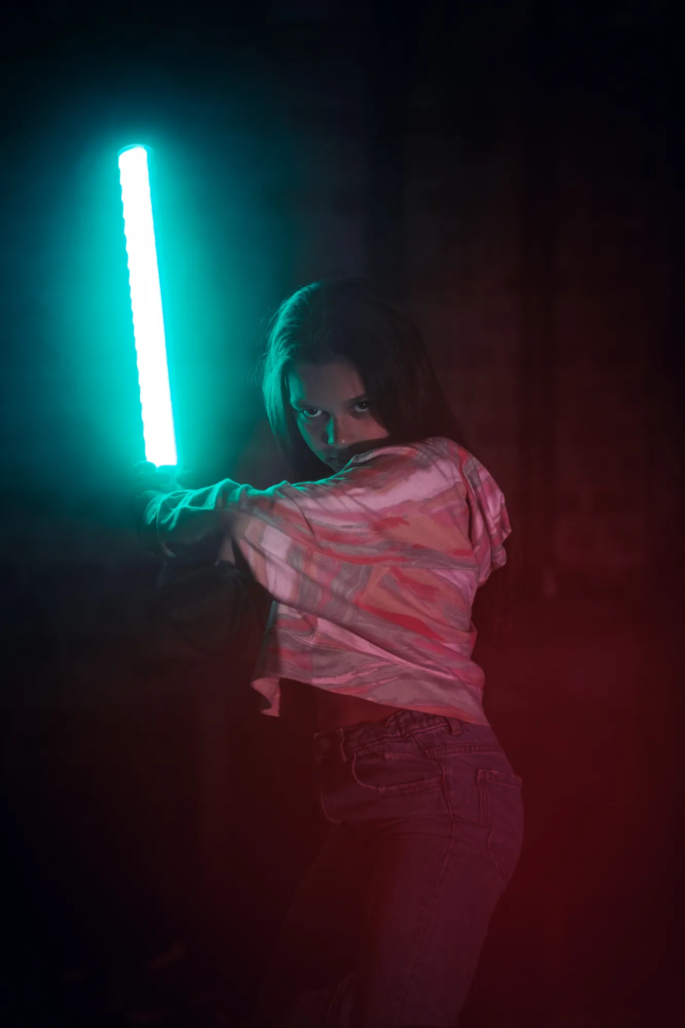 Woman aiming a cyan LED light tube in a dark smoky environment with red and teal tones